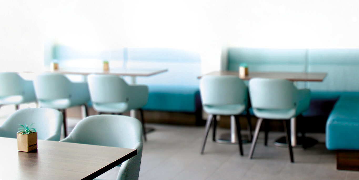 Modernes, helles Sitzbereich-Ambiente im Bistro Luise mit türkisfarbenen Bänken und Stühlen sowie gedeckten Tischen.