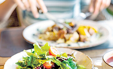 Ein frisch angerichteter Salat mit Tomaten im Bistro Luise, im Hintergrund isst ein Gast ein warmes Mittagsgericht, passend zum Text über das Speisenangebot.